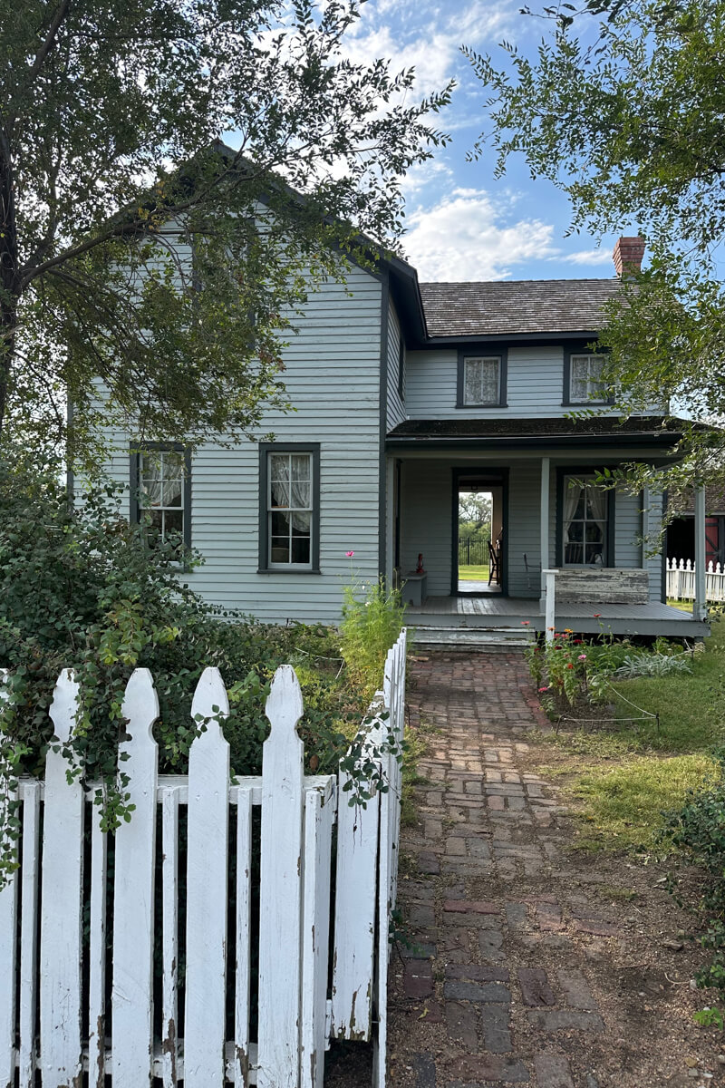 Light blue farmhouse with a porch and white picket fence