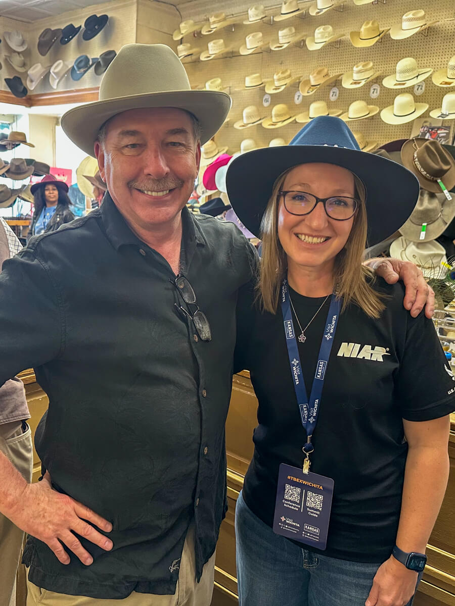 Hatman Jack in a tan hat and black shortsleeved button down shirt and a blond woman in a navy hat, black tshirt and glasses