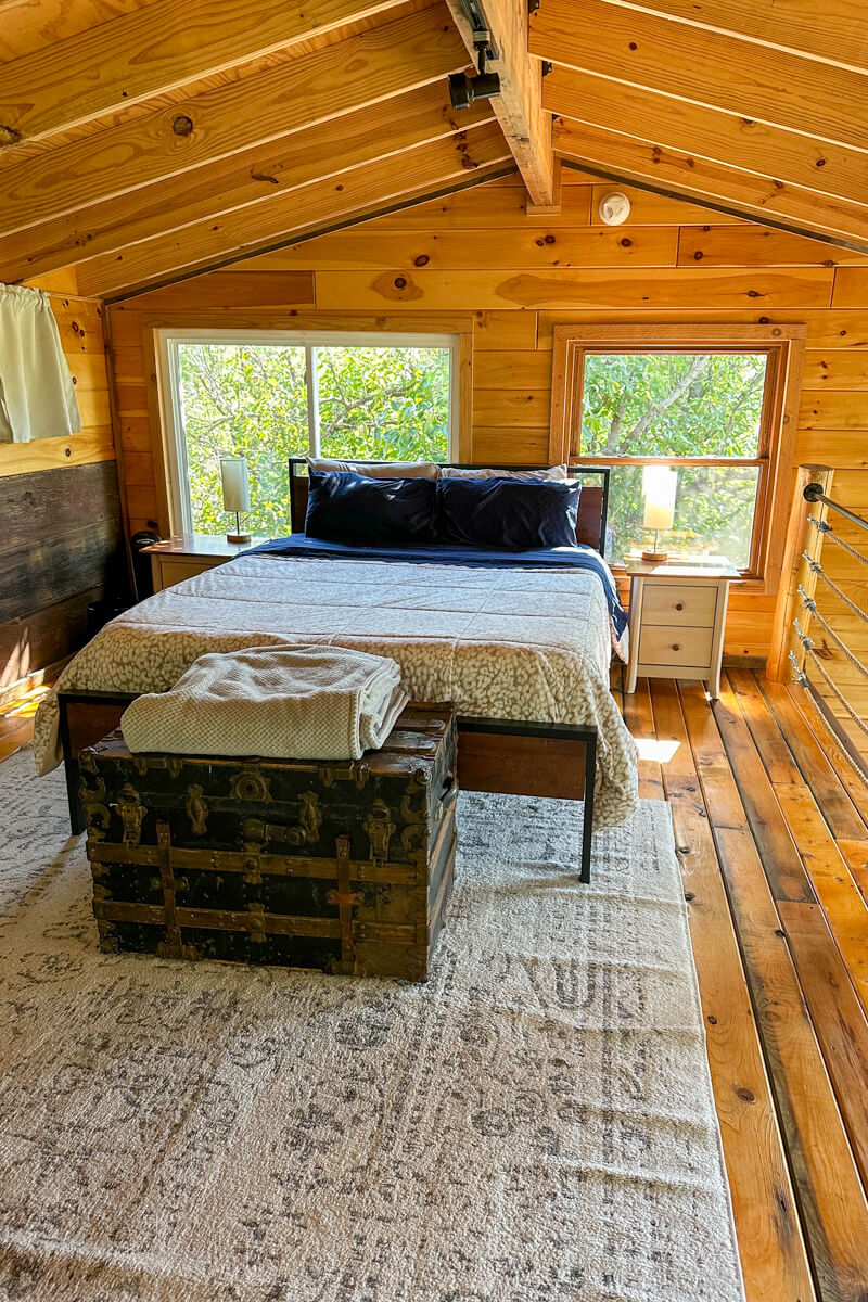 A bedroom inside the treehouse with white linens, wood floors, and walls