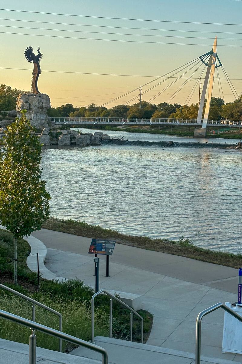 The Keeper of the Plains at twilight from a distance with the bridge next to it