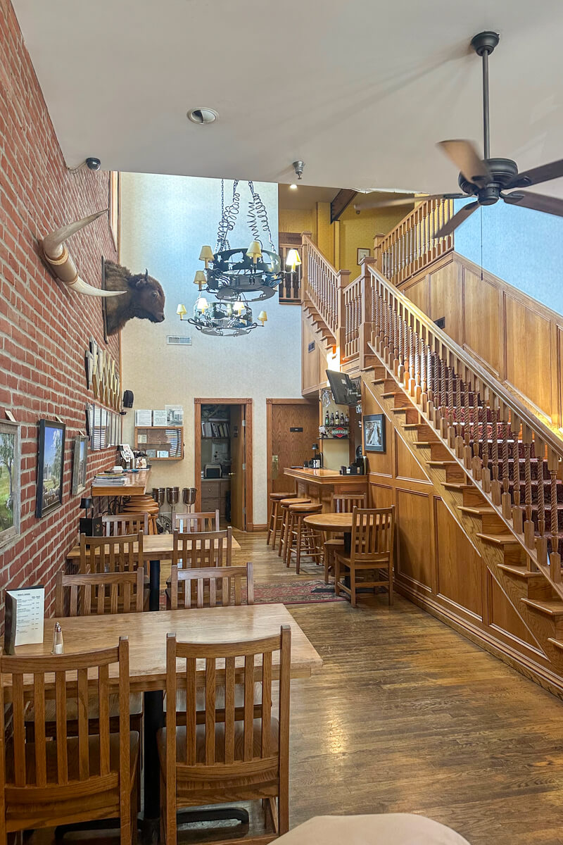 Staircase leading upstairs next to a room with wooden tables and chairs and an overhead chandelier