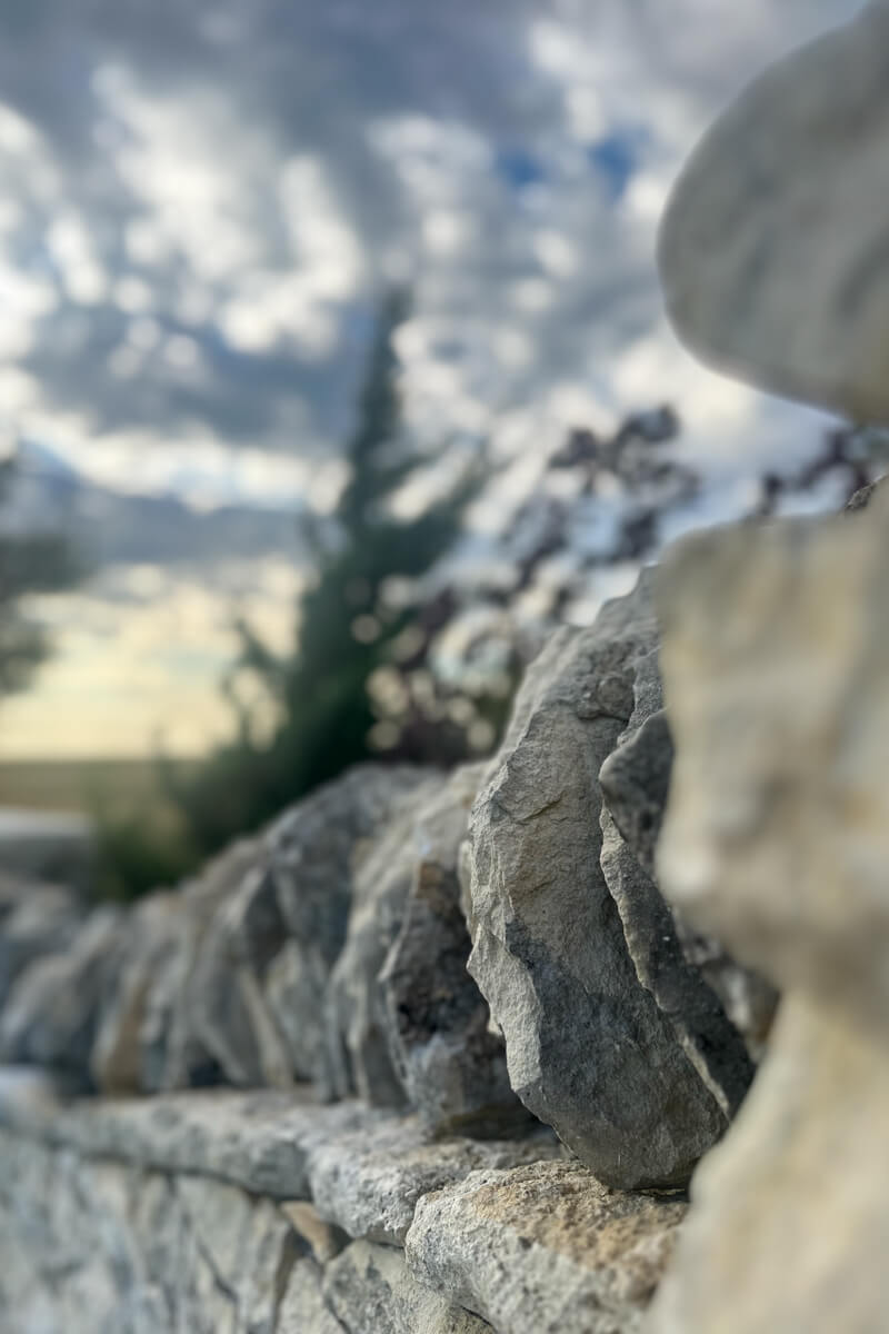 A close up view of the stone fence and clouds and trees in the backgound