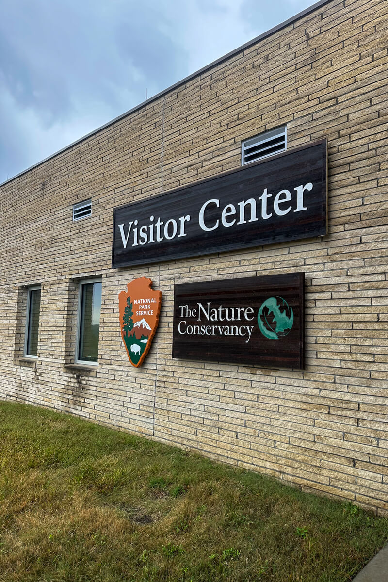 A light colored brick wall with a sign that says Visitor Center and the National Parks symbol