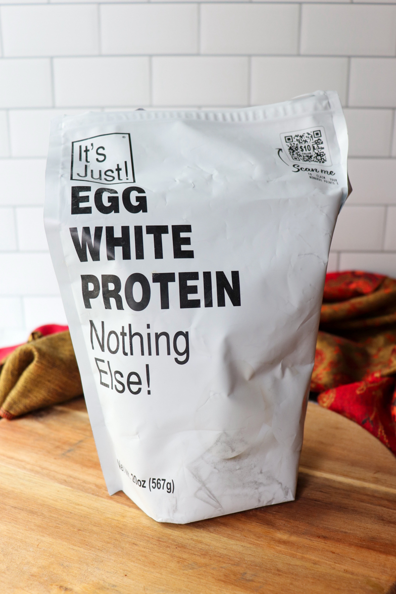 A white bag sitting on a wooden circle with black text, "It's Just! Egg White Protein Nothing Else!"