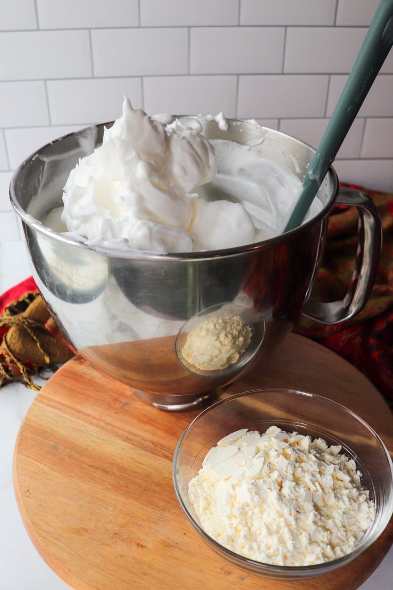 Front view of a metal bowl with a spatula stirring the whipped egg whites