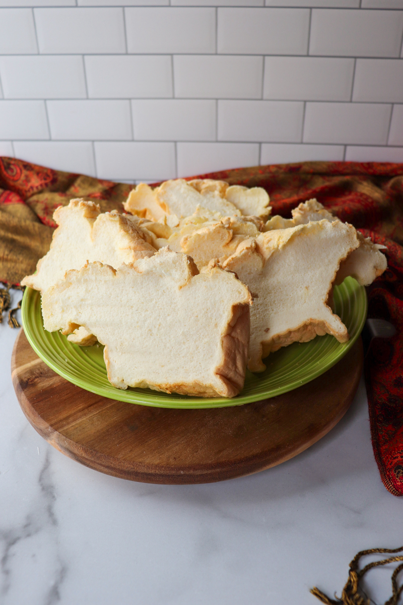 A green plate piled with slices of egg white protein bread on a wooden base