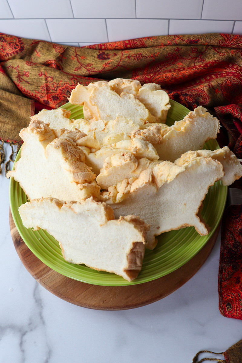 Overhead view of a green plate piled with slices of egg white protein bread on a wooden base