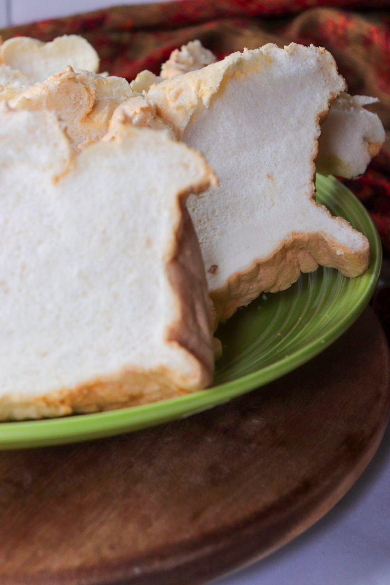Close-up front view of a green plate piled with slices of egg white protein bread on a wooden base