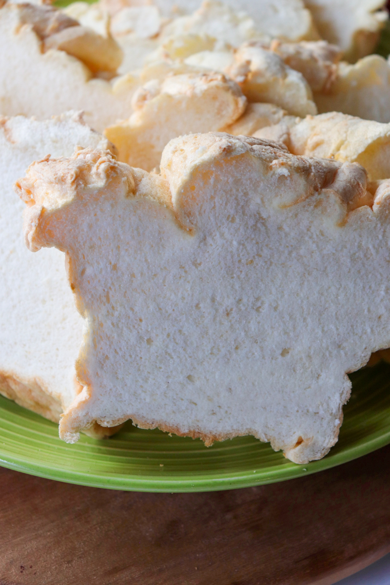 Front close up view of a green plate piled with slices of egg white protein bread on a wooden base