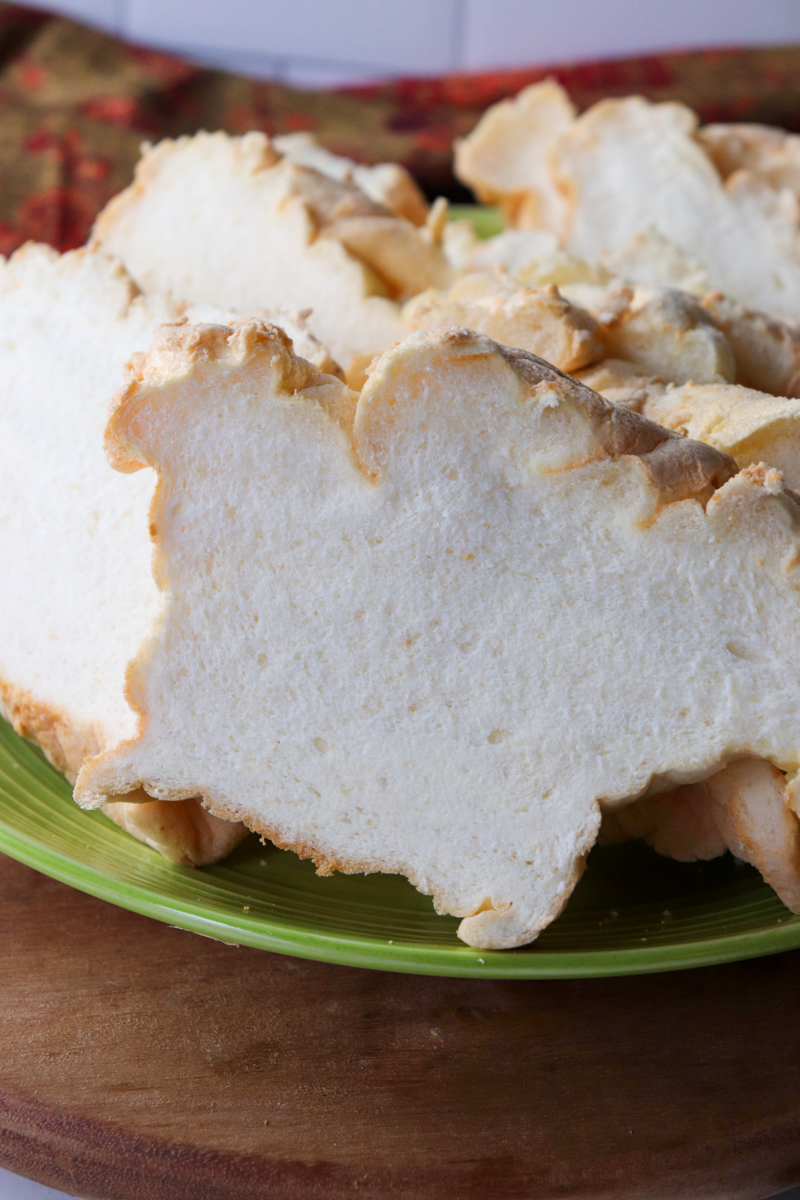Front close up view of a green plate piled with slices of egg white protein bread on a wooden base