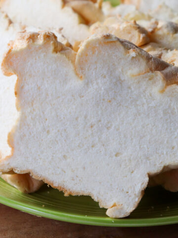 A close up of A green plate piled with slices of egg white protein bread on a wooden base