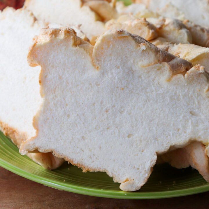 A close up of A green plate piled with slices of egg white protein bread on a wooden base