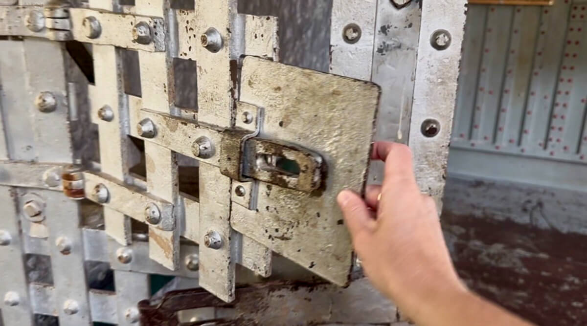 A hand reaching out toe open the food opening in the jail door