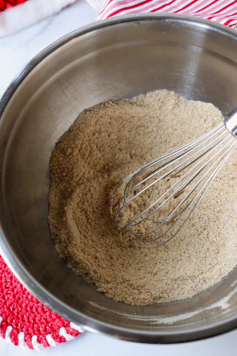 A metal bowl with a whisk stirring the dry ingredients in keto gingerbread muffin batter