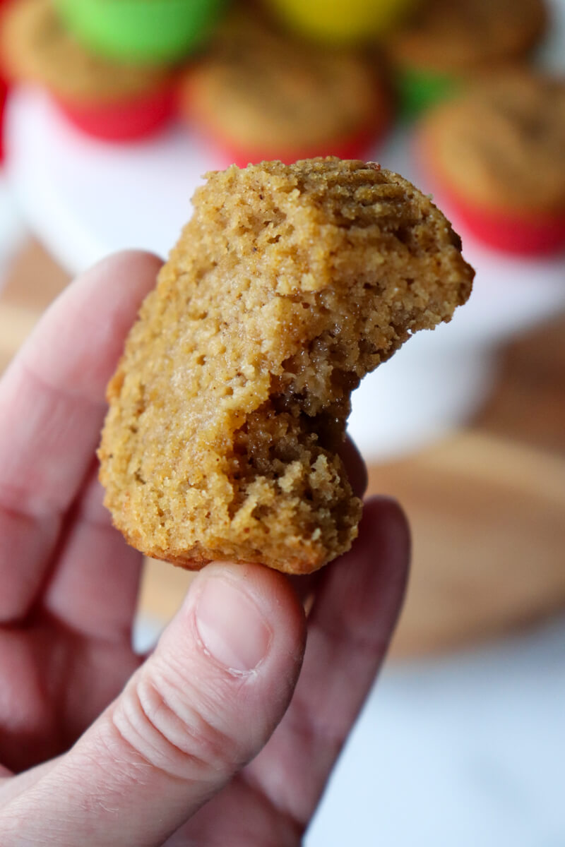 A hand holding up half of a keto gingerbread muffin with a bite taken out