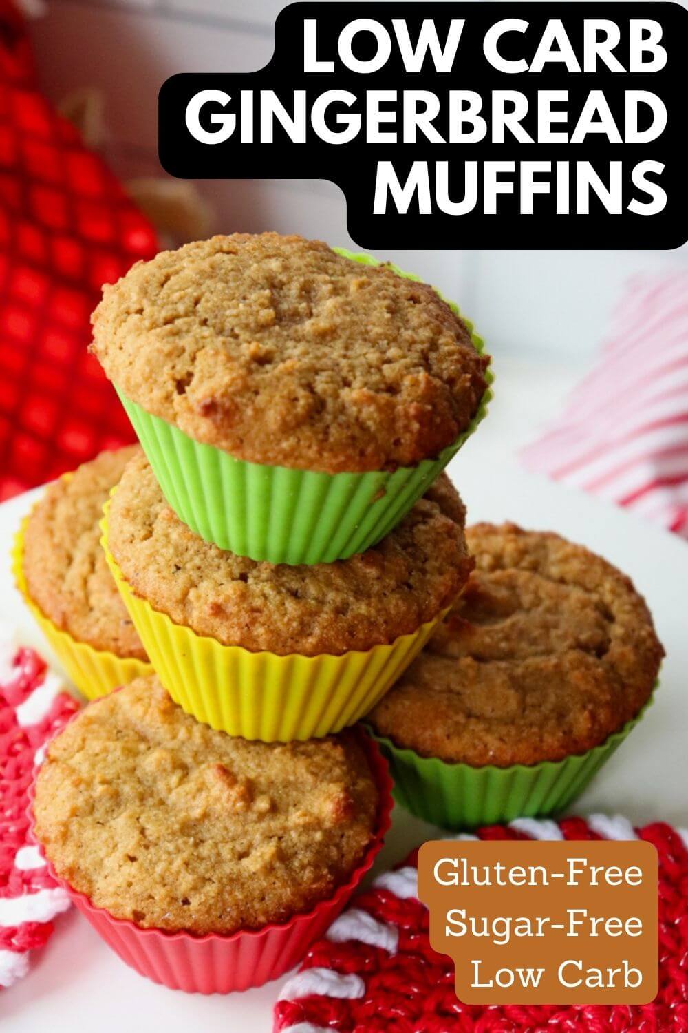A stack of keto gingerbread muffins in colored silicone cups. On a white pedestal with red and white crocheted pads. Text overlay, "Low Carb Gingerbread Muffins".