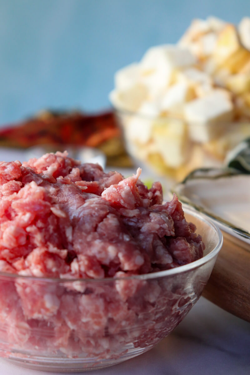 A glass bowl filled with uncooked pork sausage with cubed gluten free protein bread in the background