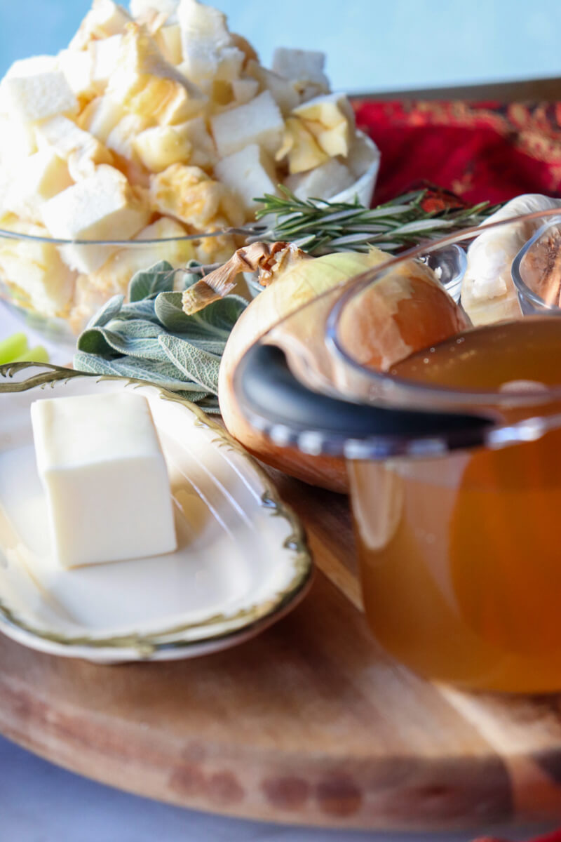 Front view of butter, chicken stock, cubed protein bread, etc. on a circular wooden serving board