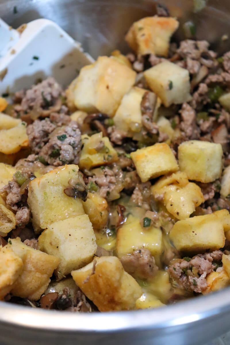 Close up of Metal bowl of sausage, sauteed veggies, and cubes of low carb protein bread with a white spatula stirring it together