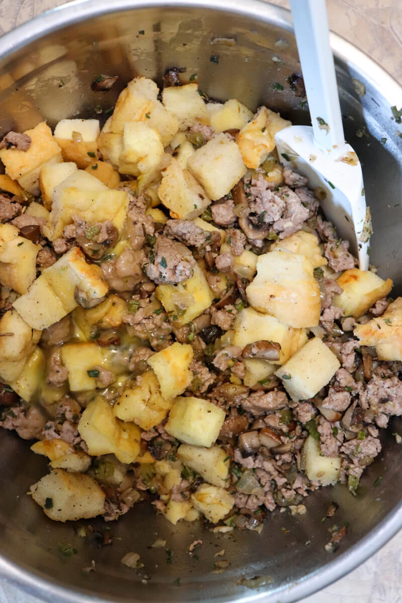 Metal bowl of sausage, sauteed veggies, and cubes of low carb protein bread with a white spatula stirring it together