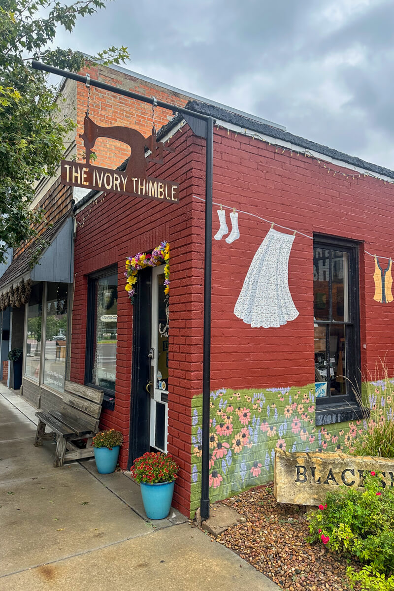 A corner brick building sewing shop with a sign in the shape of an old fashioned sewing machine and a mural of clothes outside drying on a line