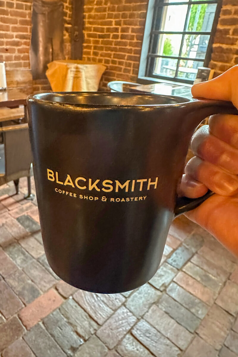 A hand holding up a black coffee mug that says "Blacksmith"