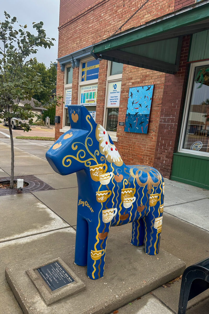 A blue Dala horse painted with coffee cups in front of a main street store
