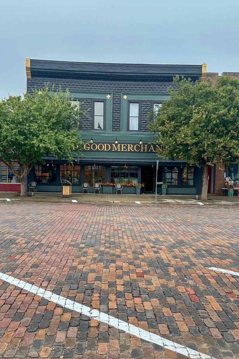 A traditional bank style building painted dark green with a cobblestone road in front of it