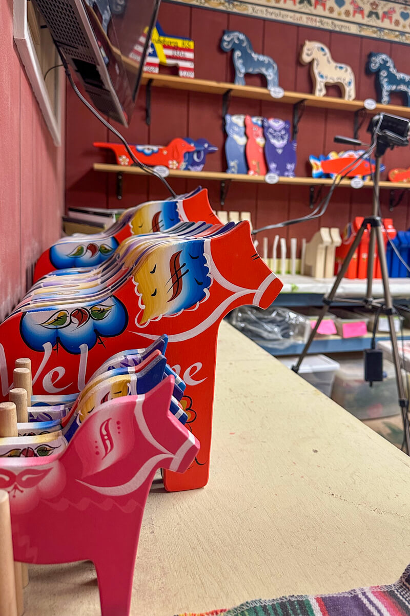 A table in the workshop with a lineup of finished red Dala horses sitting on it