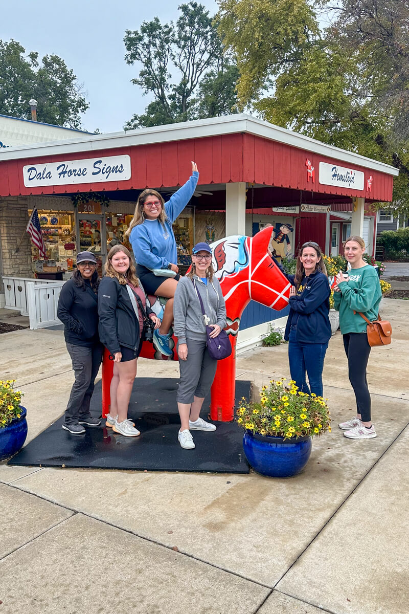 A group of women in front of a store next to a full sized red Dala horse