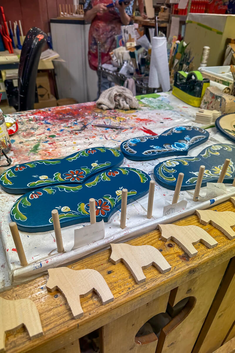 A table with blue Swedish style heart signs, a painting area, and unfinished wooden mini Dala horses