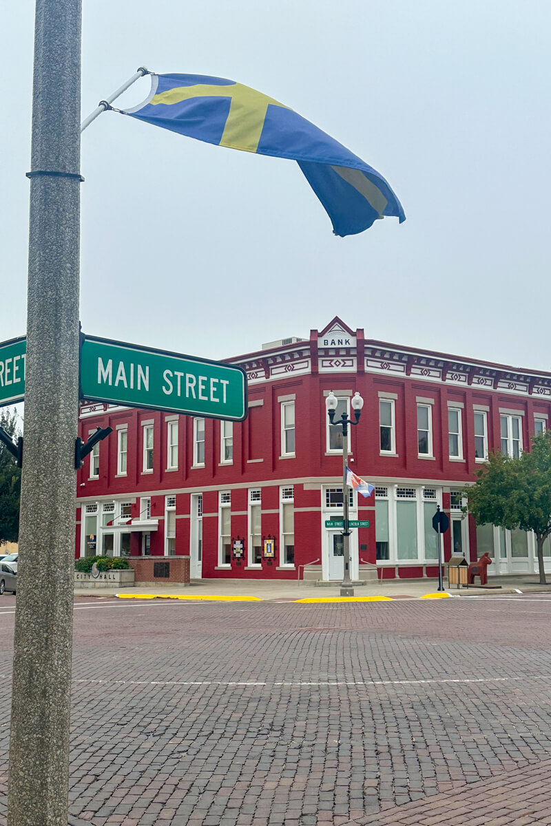 Main Street sign in Lindsborg Kansas with a red painted 2 story building in the background and a Swedish flag flying on the pole