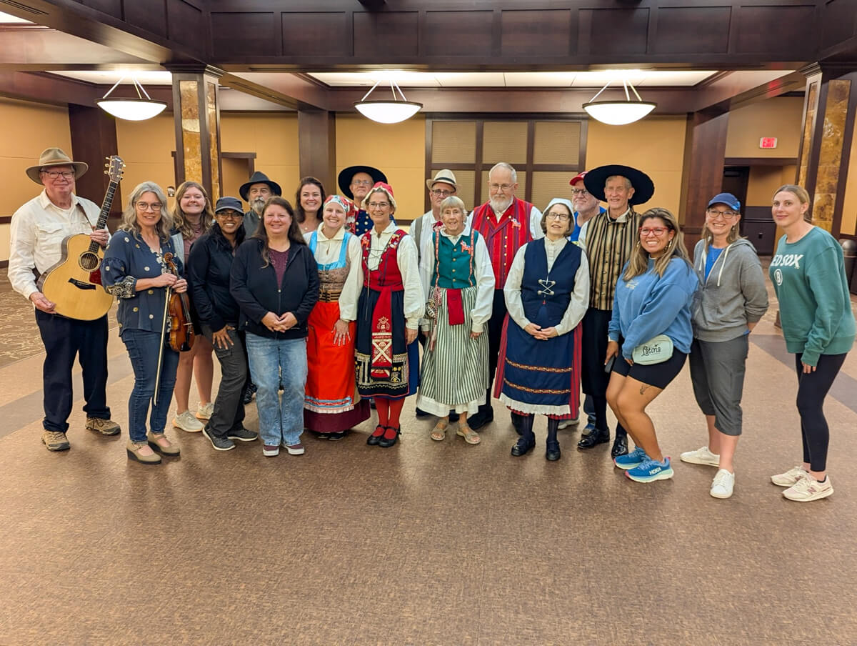 A picture of a group of people smiling at the camera, many of whom are dressed in traditional Swedish dance costumes