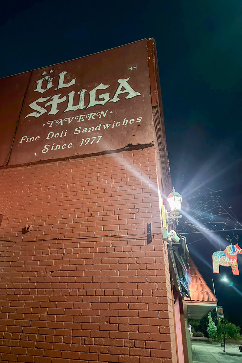 Ol Stuga painted on white on the side of a brown brick building with a Dala horse sign in front