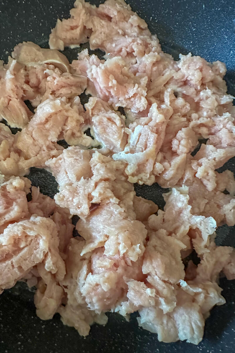 A close up view of ground chicken starting to cook in a black stovetop pan