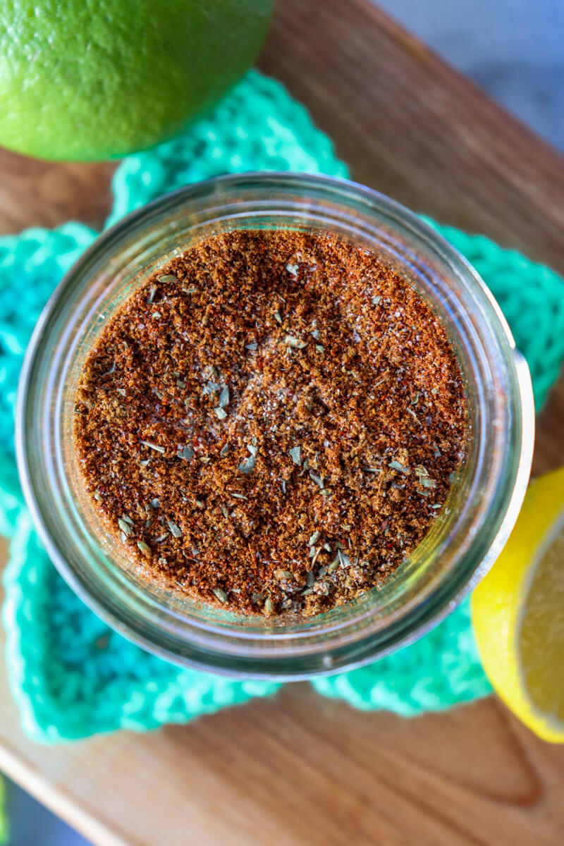 Overhead view of a glass jar of easy chicken taco seasoning on a crocheted green star coaster on a wooden cutting board next to a lime and half a lemon