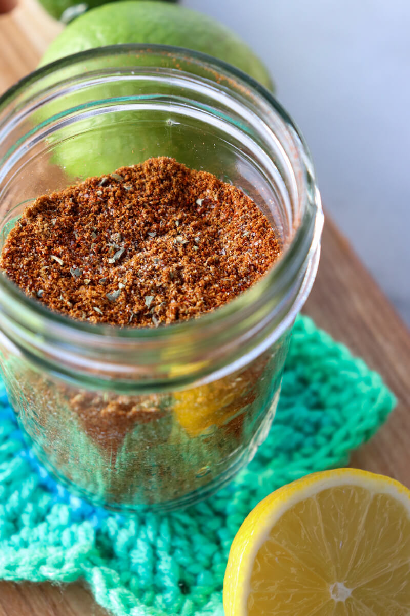 Front overhead view of a glass jar of easy chicken taco seasoning on a crocheted green star coaster next to a lime and half a lemon