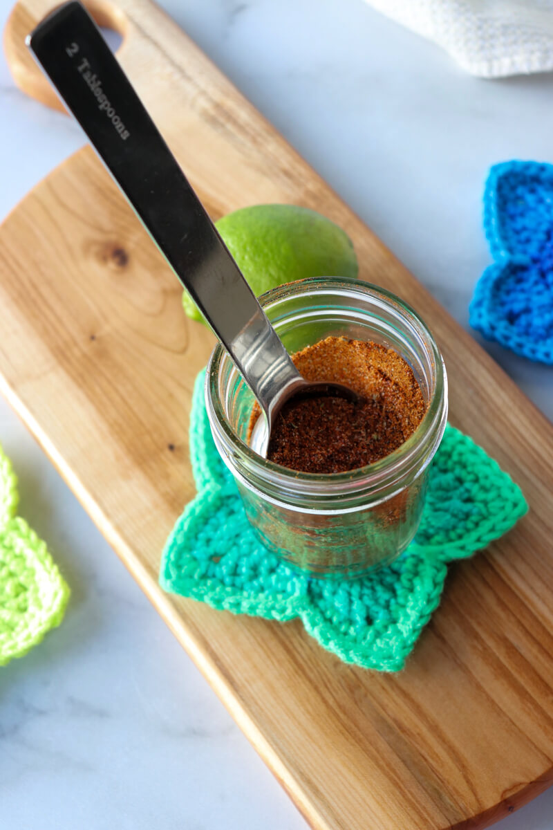Front overhead view of a glass jar of easy chicken taco seasoning on a crocheted green star coaster with a metal spoon sticking out of it