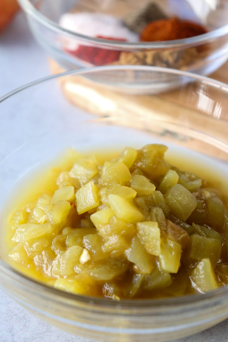 Clear glass bowl of green chilis in front of a clear glass bowl of spices