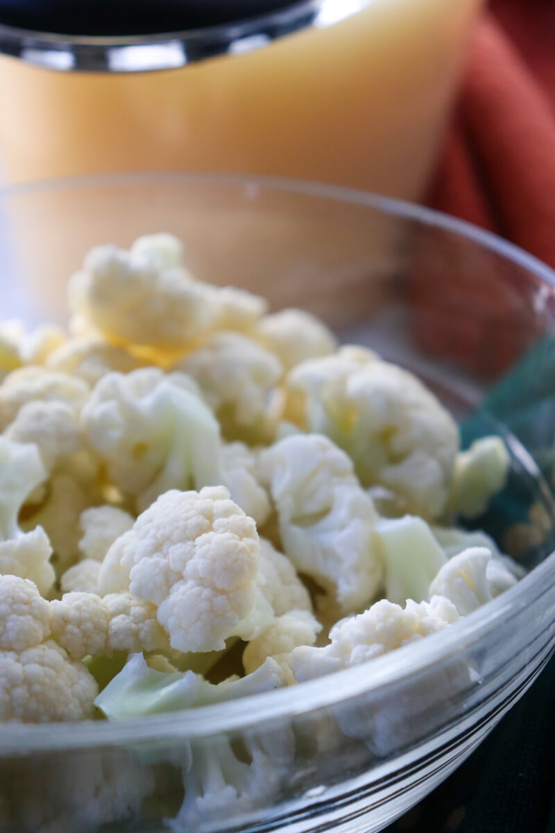 Clear glass bowl of chopped cauliflower, in front of a clear container of bone broth.