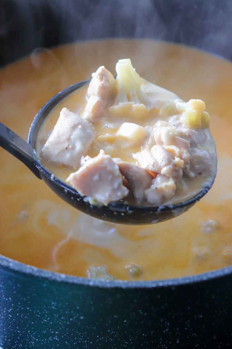 A black ladle of keto white chicken chili over a full soup pot.