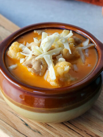 Front view of a brown ceramic bowl of keto white chicken chili with shredded Monterrey Jack cheese.