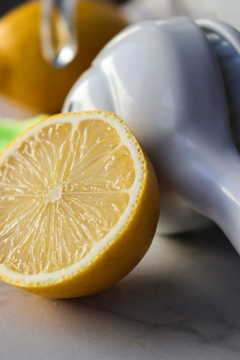 A half lemon sitting next to a white hand held citrus juicer.