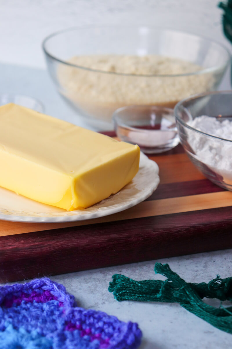 A block of yellow butter on white plate on a striped wooden cutting board with another bowl in the background