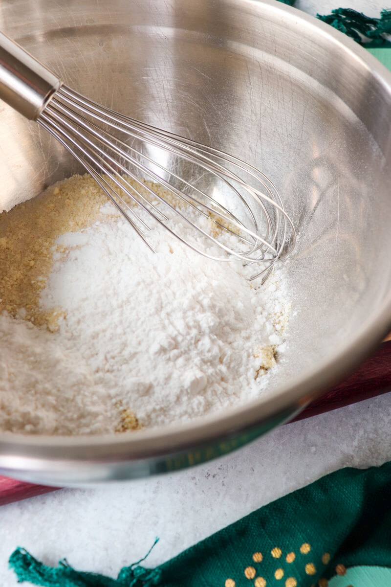 Front view of a metal bowl with gluten free shortbread dough ingredients and a metal whisk
