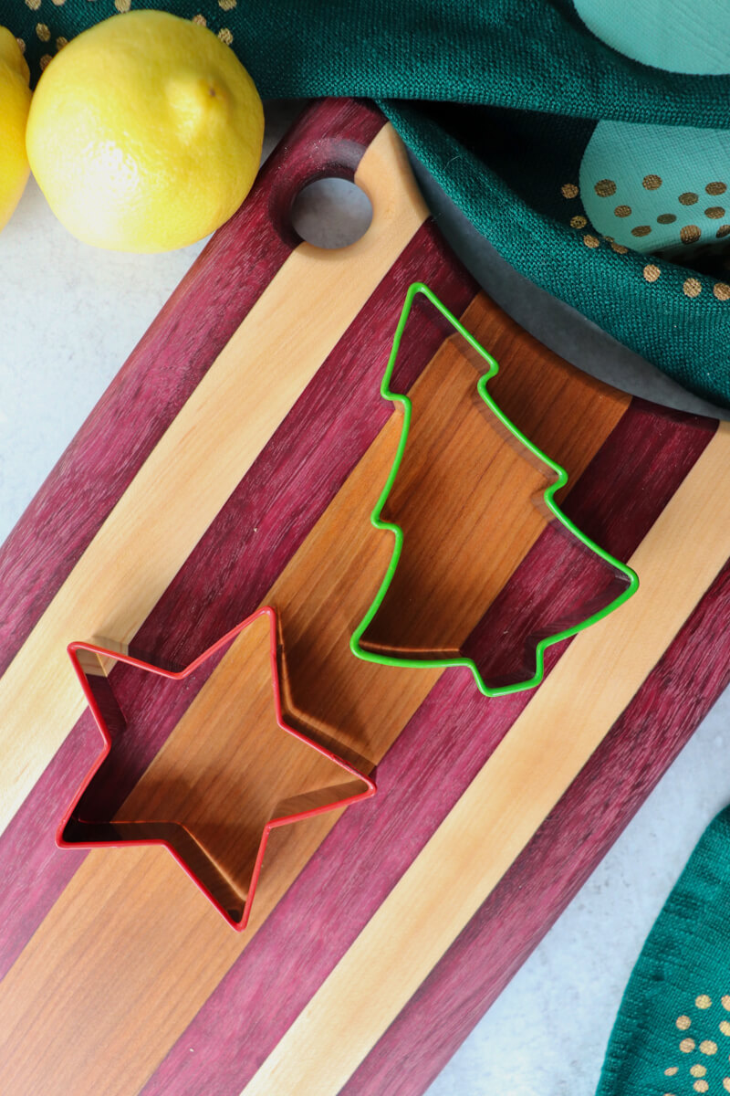 Overhead view of Christmas cookie cutters, a tree and a star, on a striped wooden cutting board