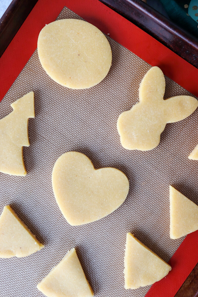 Overhead view of holiday cut out gluten free shortbread cookies on a silicone mat on a baking sheet