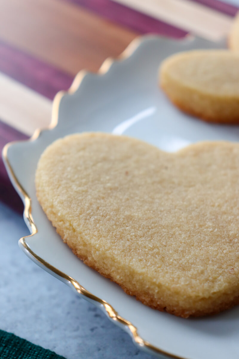 Front close up view of holiday themed cut out keto short bread cookies on a white plate, heart, with other in the background