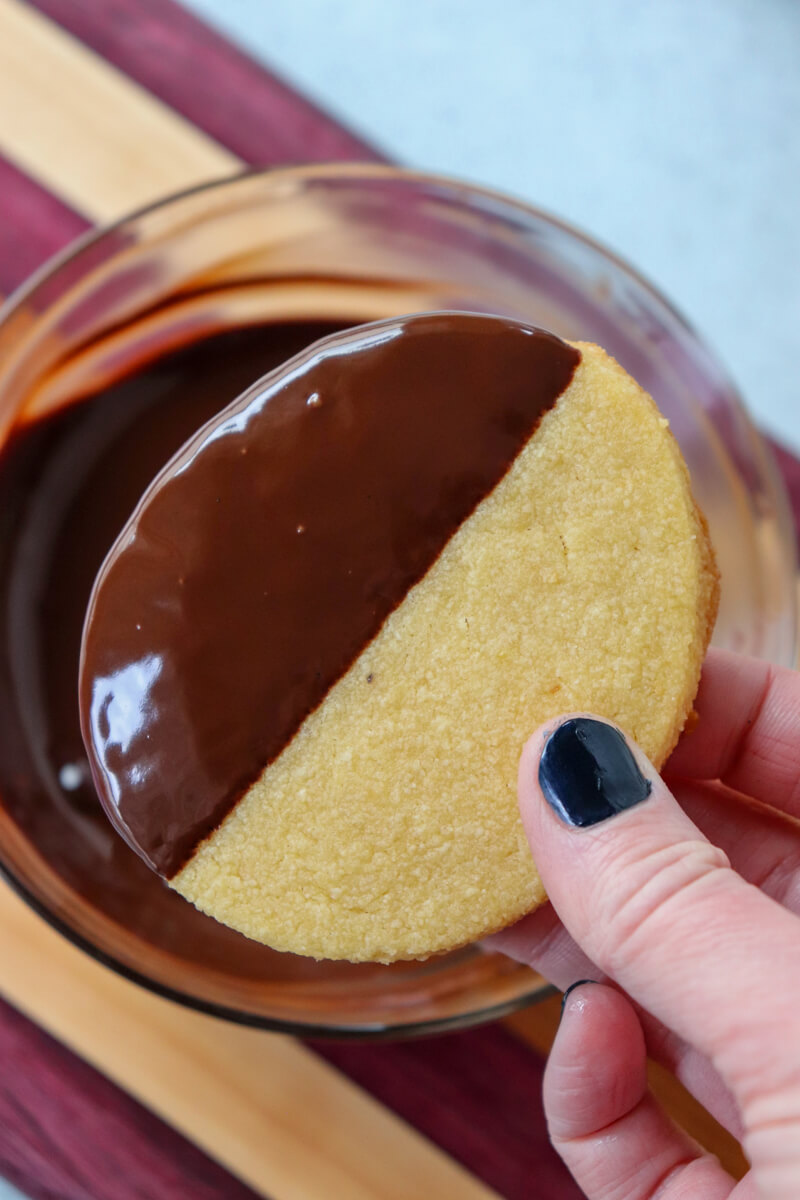 A hand dipping an egg shaped gluten free shortbread cookie in a bowl of melted chocolate