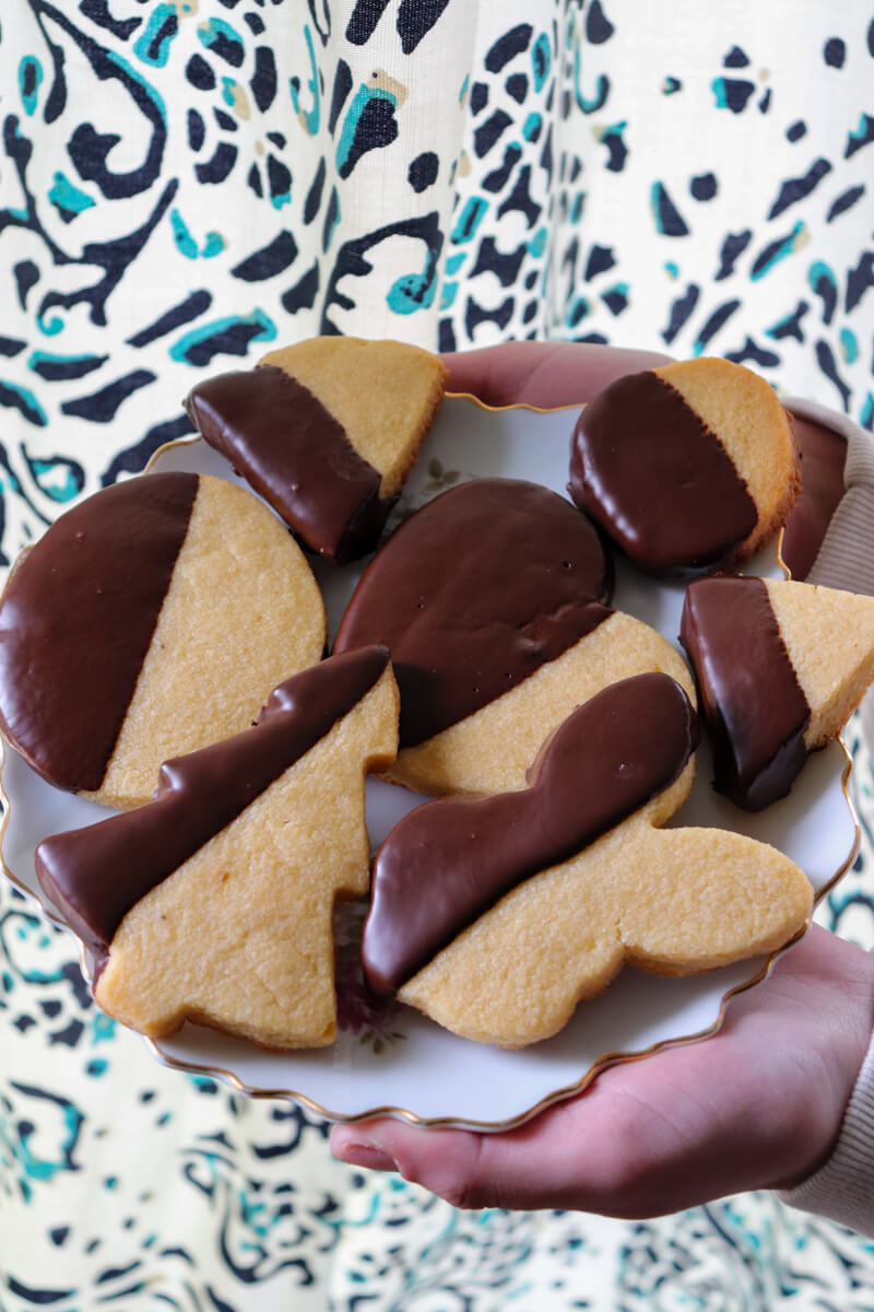 Two hands holding out a plate of gluten free shortbread cookies dipped in chocolate